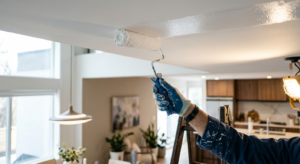A professional editorial-style shot of a painter's hand using a roller to paint a white ceiling, fea